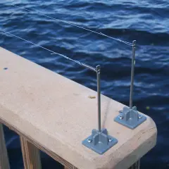 Deux piquets de pêche sur un garde-corps en bois, prêts à attraper un poisson. L'eau bleue ondule derrière.