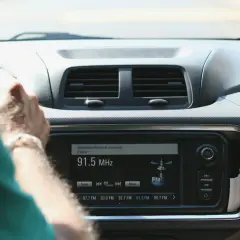 Ręce na kierownicy, radio samochodowe pokazuje 91.5 MHz. Wygodne środki masowego przekazu w podróży.