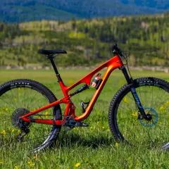 An orange Revel Ranger V2 mountain bike sits in a grassy field, ready for adventure. This revel ranger v2 review shows its sleek design.
