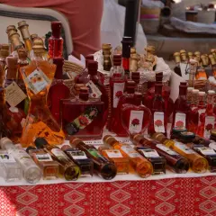 Różnorodne butelki z rakiją, w tym te w kształcie kobiecym, oferowane na targu. Co to rakija? To tradycyjny alkohol, często owocowy.