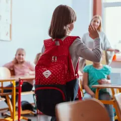 Dziewczynka z czerwonym plecakiem w klasie, może odczuwać lęki u dziecka 7 latka, ale nauczycielka i koledzy dodają jej otuchy.