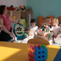 W przedszkolu opiekunka dba o kilkoro dzieci bawiących się zabawkami.