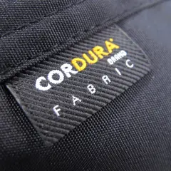 Czarna tkanina z naszywką "CORDURA FABRIC". Materiał ten, znany ze swojej wytrzymałości, często wykorzystywany jest w produktach outdoorowych, jak plecaki czy torby.