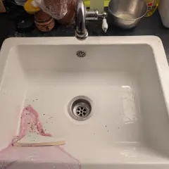 Un évier blanc avec un robinet chromé. Un outil blanc est utilisé pour aider à comment enlever un évier collé au silicone.