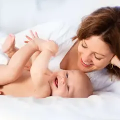 Uśmiechnięta mama patrzy na radosne dziecko leżące na białym tle.