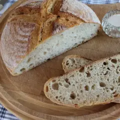 Chleb żytni na zakwasie, przekrojony na desce, z kilkoma kromkami i solniczką.