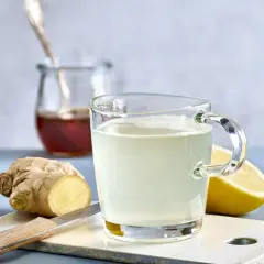 Ingwer Zitrone Tee selber machen: Ein Glas frisch aufgebrühter Tee mit Zitrone und Ingwer, daneben frischer Ingwer, Zitrone und ein Glas Honig.