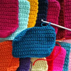 Uncinetto in azione su un lavoro a maglia colorato. Si intravede una sciarpa uncinetto morbida in lavorazione, con fili di lana vivaci.