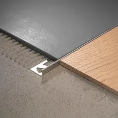 Détail d'un raccord de sol entre carrelage gris et parquet bois, avec une plinthe métallique.