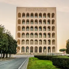 Il Colosseo Quadrato, imponente edificio con arcate sovrapposte, si erge maestoso tra alberi verdi e un cielo tenue.