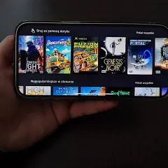 Ręka trzyma smartfon z grami do samolotu. Widoczne okładki gier: DUSK, Overcooked! 2, Fuzion Frenzy, Genesis Noir, Bridge Constructor Portal, High On Life, Halo Infinite, Forza Horizon, Sea of Thieves.