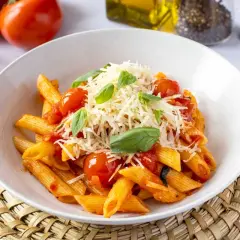 Un plato de macarrones a la napolitana, con salsa de tomate, tomates cherry, albahaca fresca y queso rallado.