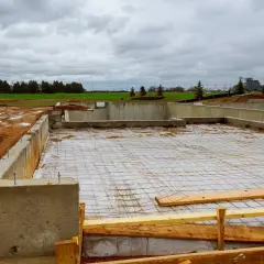 Fundament betonowy w budowie, z widocznymi zbrojeniem i folią. Trudno oszacować ile bloczków betonowych na fundament zużyto.
