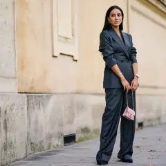 Elegancka kobieta w garniturze w **gołębi kolor** i różową torebką na łańcuszku.