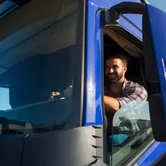 Uśmiechnięty kierowca ciężarówki w kratę. Czy jego praca to 10 godzin jazdy ile razy w tygodniu?