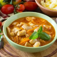 Aromatyczny gulasz z piersi kurczaka z marchewką, udekorowany bazylią. Obok miska z purée ziemniaczanym i kromki chleba.
