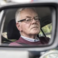 Älterer Mann mit Brille im Rückspiegel, der sich fragt, warum das Auto quietscht.