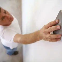 Un homme ponce un mur blanc avec une cale à poncer. C'est une étape essentielle : faut-il poncer un mur avant de le peindre pour un fini parfait ?
