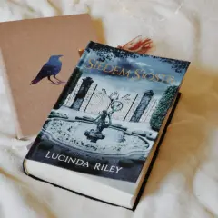 Książka "Siedem Sióstr" Lucindy Riley na tle okładki z ptakiem.