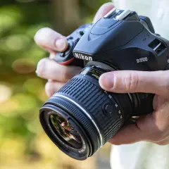 Mani che impugnano una Nikon D3500 con obiettivo 18-55mm. Dettagli sulla nikon d3500 scheda tecnica.