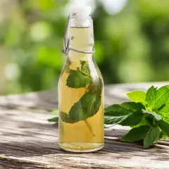 Bouteille de sirop de menthe maison avec des feuilles de menthe fraîche sur une table en bois.