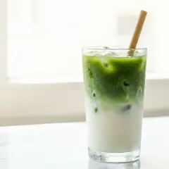 Un cocktail matcha glacé, avec du lait et une paille en bambou, sur un fond lumineux.