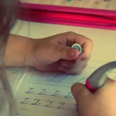 Niño/a practicando caligrafía en un cuaderno con letras cursivas.