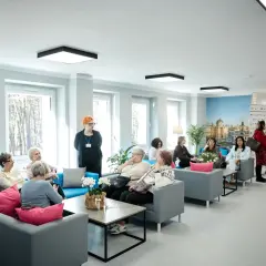 Grupa seniorów siedzi na kanapach w jasnym, nowoczesnym wnętrzu domu opieki.