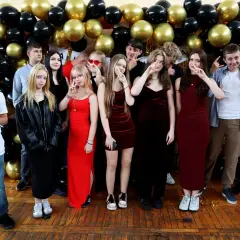 Uczniowie pozują do zdjęcia na tle balustrady z czarnych i złotych balonów. To ważny moment, być może zakończenie roku szkolnego lub studniówka.