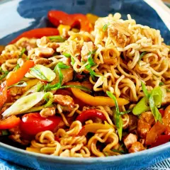 Schüssel mit Nudeln, Paprika, Frühlingszwiebeln und Hühnchen. Ein Teller mit einfachen asiatischen Gerichten, bereit zum Genießen mit Stäbchen.