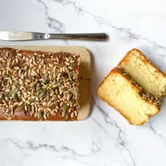 Plumcake senza uova, soffice e dorato, ricoperto di semi misti. Due fette tagliate mostrano la sua morbidezza.