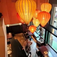 Interno di un ristorante cinese a Milano, illuminato da lanterne orientali. Una donna osserva l'ambiente.