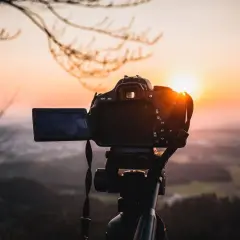 Aparat fotograficzny na statywie, gotowy do uchwycenia zachodzącego słońca nad doliną. Solidna podstawa aparatu zapewnia stabilność.