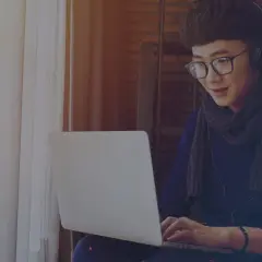 Jeune homme avec des écouteurs et des lunettes travaille sur son ordinateur portable, rédigeant une lettre de motivation intérim sans expérience.