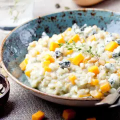 Cremiges Kürbis-Risotto mit Blauschimmelkäse und Pinienkernen. Ein Glas Wasser steht bereit, perfekt zum Genießen dieses Risotto, welcher Wein passt wohl dazu?