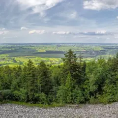 Widok z góry na zielone pola i lasy, idealne na fajne miejsca w świętokrzyskim na weekend. Kamieniste zbocze i chmury na niebie.