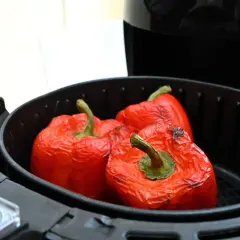 Peperoni rossi interi cotti nella friggitrice ad aria, con la buccia leggermente raggrinzita e qualche macchia scura.