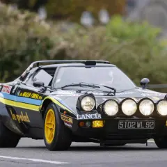 Czarny Lancia Stratos z żółtymi felgami i rajdowymi oznaczeniami, gotowy do pokonania kolejnego zakrętu.