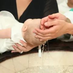 Chrzest dziecka. Woda spływa po głowie malucha. Ile się daje na chrzest, to już inna sprawa.
