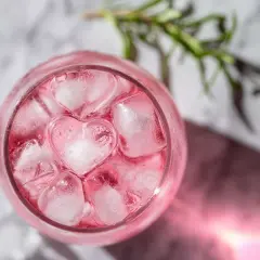 En rosa drink med hjärtformade isbitar och en rosmarinkvist.