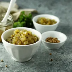 En skål med finhackad bostongurka, perfekt för ditt bostongurka recept. Bredvid en burk med gurka och en skål med senapsfrön.