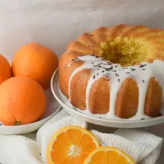 Bizcocho de naranja y yogur con glaseado blanco y chispas de chocolate. Naranjas frescas y rodajas de naranja completan la escena.