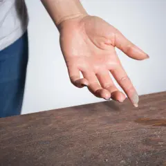 Mano con polvo en la yema del dedo, sobre una mesa de madera. Un recordatorio visual de cómo evitar el polvo en la habitación.
