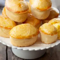 Un mucchio di pasticciotti leccesi dorati e invitanti su un'alzata bianca, pronti per essere gustati.