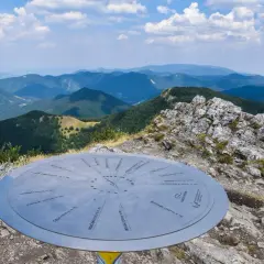 Widok z klak szczyt na pasmo górskie. Na pierwszym planie metalowa tablica z nazwami szczytów.