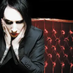 Marilyn Manson, z charakterystycznym makijażem, siedzi na aksamitnej kanapie. Jego utwory często poruszają mroczne tematy.
