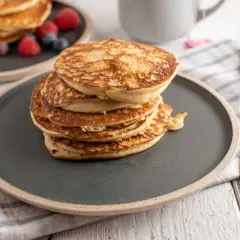Stos puszystych fit pancakes z odżywki białkowej, ozdobiony malinami i borówkami, czeka na widelcu.
