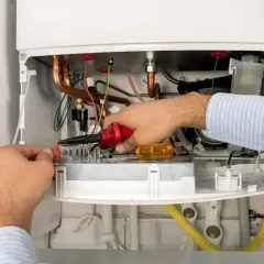 Technik przeprowadza przegląd piecyka gazowego, manipulując przewodami za pomocą szczypiec.