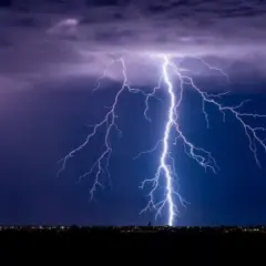 Un rayo ilumina el cielo nocturno, como si fuera un sueño con tormenta. Las nubes púrpuras y el horizonte iluminado por luces de ciudad crean una escena dramática.