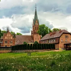 Majestatyczne sanktuarium w Gietrzwałdzie, z ceglaną architekturą i strzelistą wieżą, góruje nad zieloną łąką pełną kwiatów.